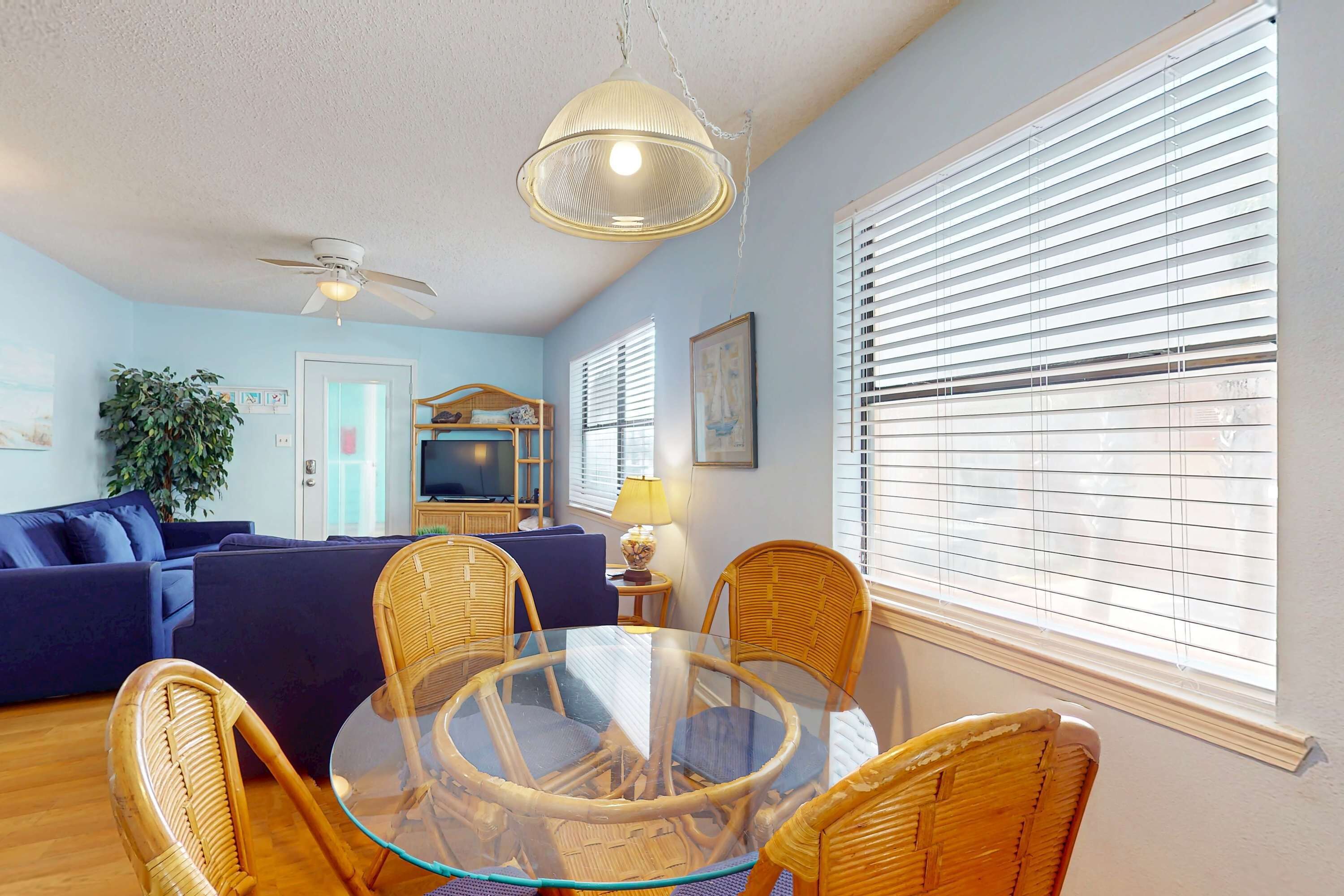 A living room with a glass table, wicker chairs, a blue sofa, and a ceiling fan.
