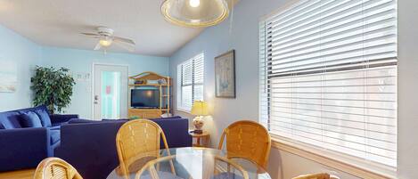 A living room with a glass table, wicker chairs, a blue sofa, and a ceiling fan.