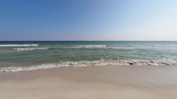 Ein Strand mit Wellen, blauem Himmel und ruhiger See.