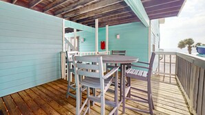 Eine überdachte Außenfläche mit einer Holzterrasse, einem Tisch mit Stühlen und einer Treppe, die zu einer erhöhten Ebene führt.