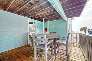A covered outdoor area with a wooden deck, a table with chairs, and a staircase leading to an upper level. - Waterfront condo with a furnished balcony, peek-a-boo Gulf views, & shared pools (Gulf Shores)