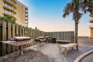 A patio area with a grill, seating, and a wooden fence. - Gulf-Front Condo w Beach Access, WiFi, Balcony & Shared Pools, Hot Tubs & Gym (Gulf Shores)
