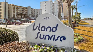 Opastekyltti, jossa lukee ”Island Sunrise”, ja sen alla numero ”427”. Taustalla näkyy parkkipaikka ja rakennuksia.