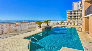 Piscina no terraço com vista clara do oceano, cercada por um muro branco, e um prédio com sacadas.