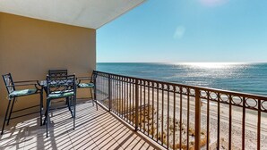 Uma varanda com vista para o oceano, uma mesa com cadeiras e um corrimão.