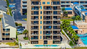 Um hotel com vários andares, varandas, piscina e estacionamento.