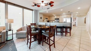 Cozinha moderna com ilha central, cadeiras de madeira, mesa de jantar e ventilador de teto.