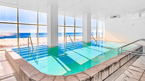 Piscina interna com vista direta para a praia e oceano através de grandes janelas.