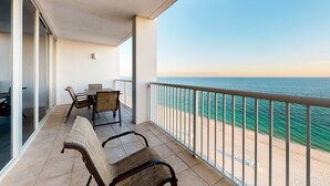 Varanda com vista para o mar, uma mesa com cadeiras e uma porta de vidro que dá para um espaço interior.