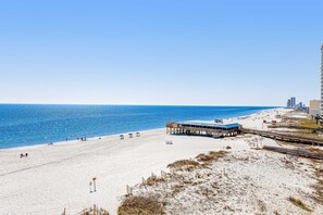 Una platja amb un moll, sorra daurada i un cel blau clar.