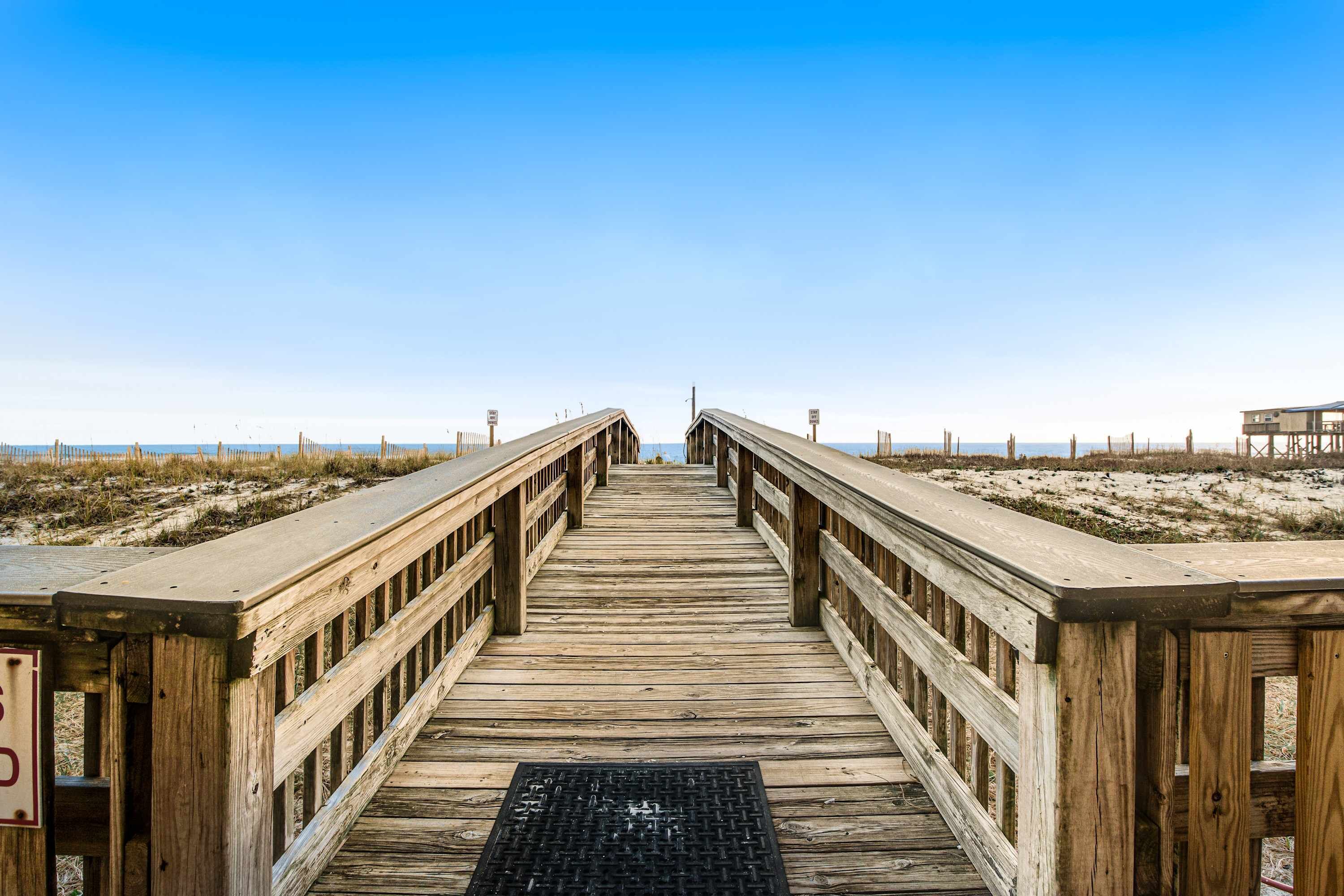 En træpromenade der fører til en strand med en klar himmel.