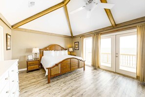 A bedroom with a wooden bed, a nightstand, a dresser, and a large window with curtains. - Beachfront house with balcony, deck, ocean view, central AC, & washer/dryer (Gulf Shores)