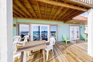A covered outdoor area with a wooden deck, a table, and chairs. - Beachfront house with balcony, deck, ocean view, central AC, & washer/dryer (Gulf Shores)