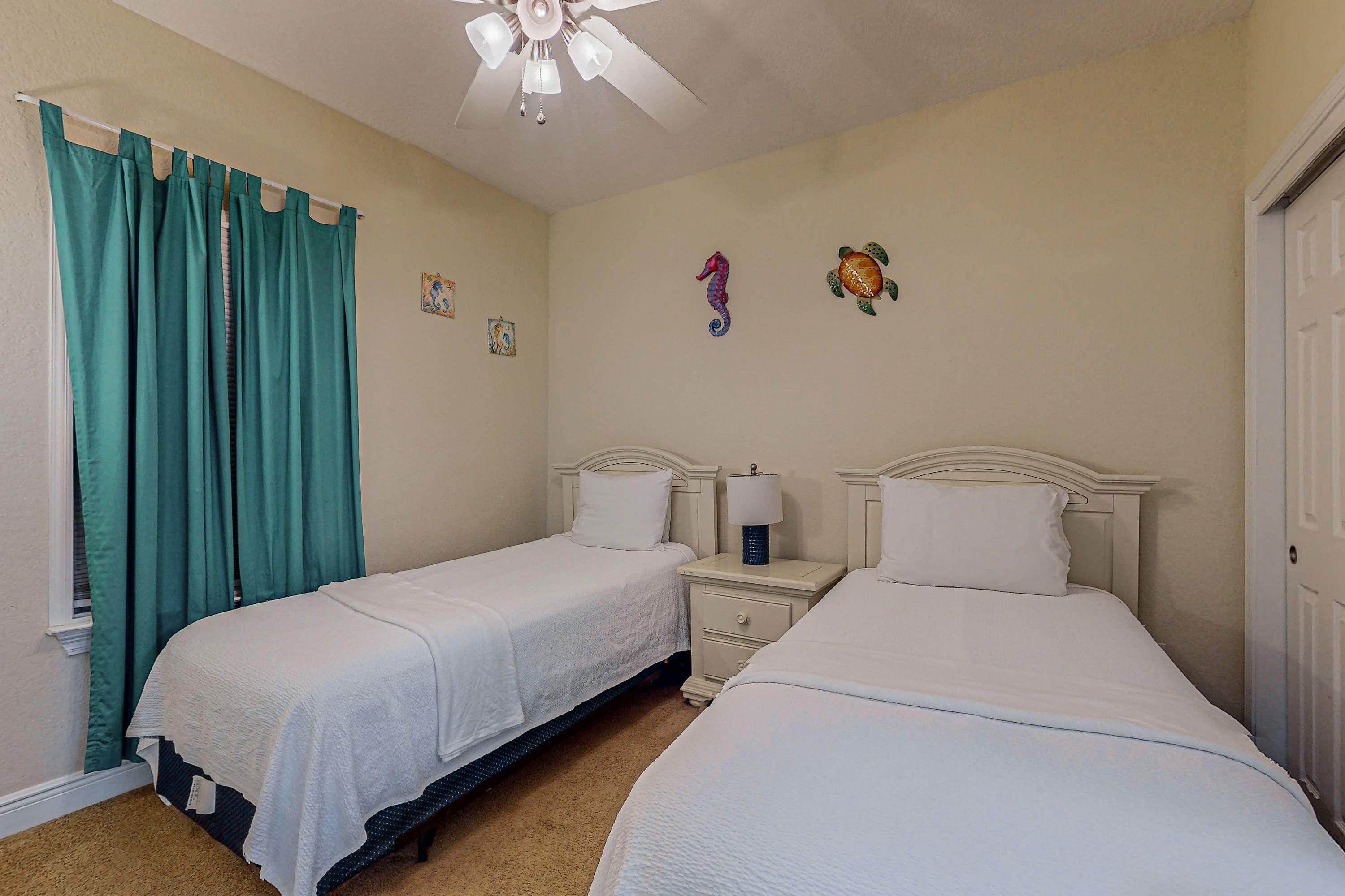 Une chambre d’hôtel avec deux lits, un ventilateur de plafond et une fenêtre avec des rideaux de couleur turquoise.