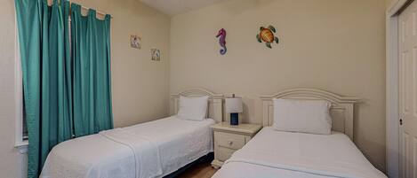 Une chambre d’hôtel avec deux lits, un ventilateur de plafond et une fenêtre avec des rideaux de couleur turquoise.