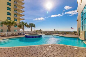 A swimming pool with a hot tub, palm trees, and a view of the ocean. - Incredible oceanfront condo with balcony, AC, pool, gym & hot tub (Gulf Shores)