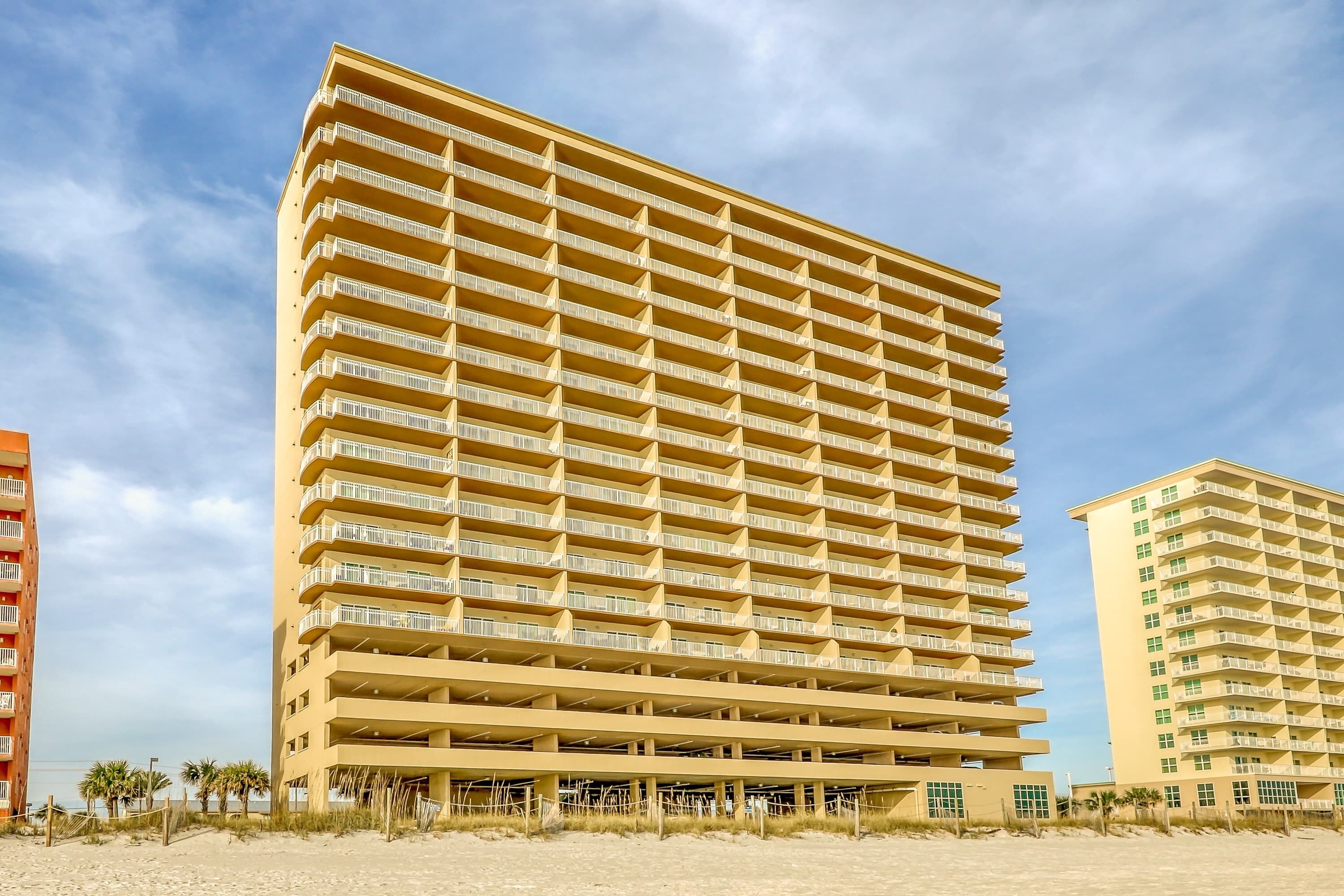 A high-rise hotel with multiple balconies, a flat roof, and a sandy beach in the foreground.