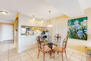 A modern kitchen with white cabinets, a stainless steel refrigerator, and a dining area with a glass table and metal chairs. - 6th-Floor waterfront condo with pool & balcony - snowbird-friendly (Gulf Shores)