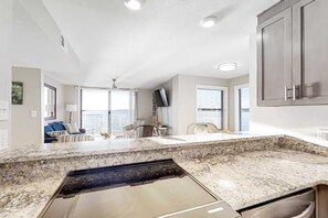 A modern kitchen with granite countertops, a built-in dishwasher, and a large window providing natural light. - Lagoon-front, 3rd-floor condo with balcony, AC, & outdoor pool (Gulf Shores)