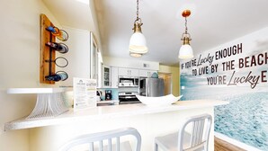 A modern kitchen with a bar area, a wooden wine rack, and a kitchen island with two chairs. - Beachfront home with furnished waterfront deck, balcony, & central AC (Gulf Shores)