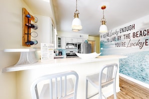 A modern kitchen with a bar area, a wooden wine rack, and a kitchen island with two chairs. - Beachfront home with furnished waterfront deck, balcony, & central AC (Gulf Shores)