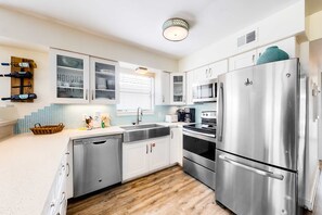 A modern kitchen with stainless steel appliances, white cabinetry, and a wooden floor. - Beachfront home with furnished waterfront deck, balcony, & central AC (Gulf Shores)