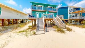 A beachfront property with a multi-level building, wooden walkways, and a sandy beach. - Beachfront home with furnished waterfront deck, balcony, & central AC (Gulf Shores)