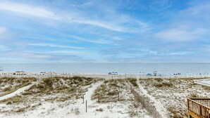 A beach view with a wooden deck, sandy dunes, and a clear sky. - Beachfront home with furnished waterfront deck, balcony, & central AC (Gulf Shores)