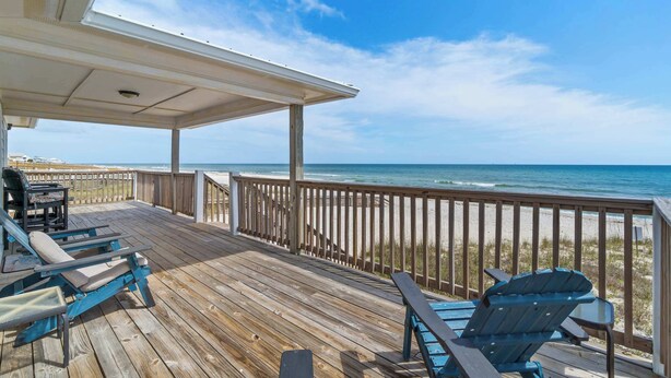 Eine Holzterrasse mit Geländer, mit Blick auf einen Strand und den Ozean.