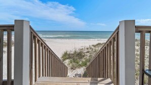 Eine Holztreppe führt zu einem Strand unter blauem Himmel.