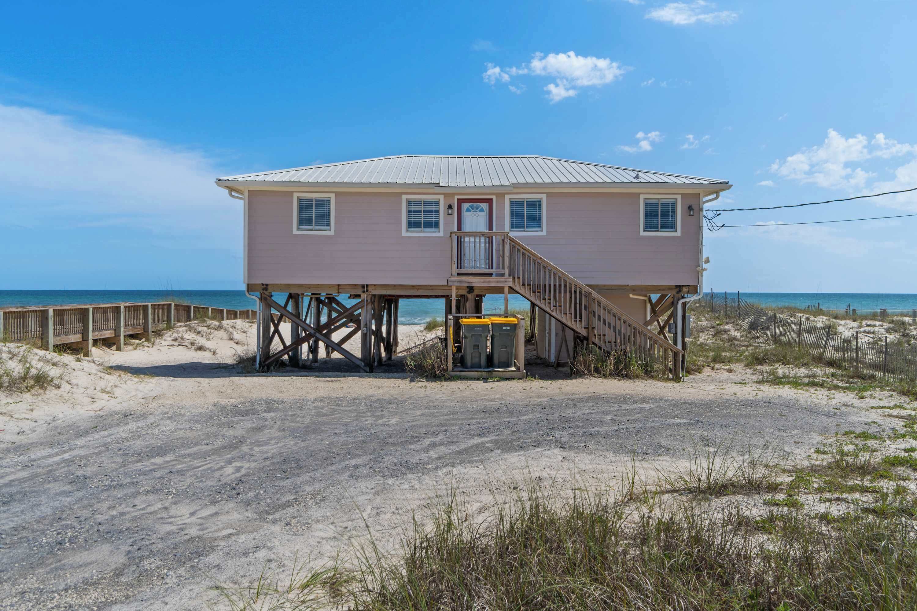 A beach house with a wooden deck, a staircase, and a view of the ocean.
