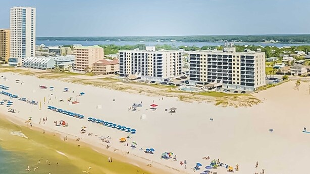 Ein Hotel direkt am Strand mit mehreren Gebäuden, einem Sandstrand und zahlreichen Sonnenschirmen.