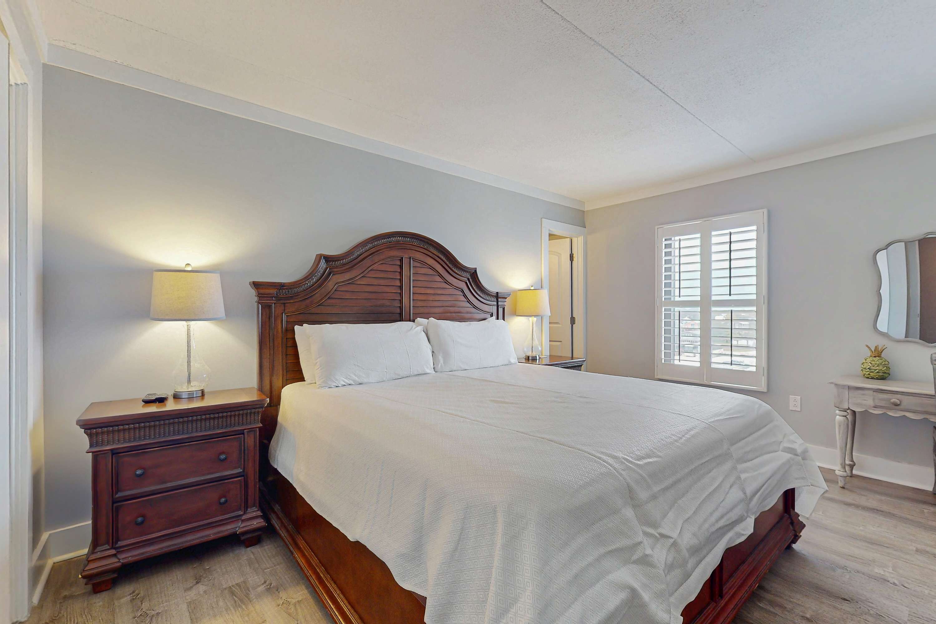 A bedroom with a large bed, a nightstand, a lamp, a dresser, and a window with blinds.