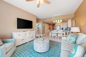 A living room with a television, white furniture, a round coffee table, and a patterned rug. - Gulf-Front Condo w/ Beach View, Balcony, AC & Resort Pools/Hot Tubs/Sauna (Gulf Shores)