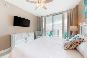 Une chambre d’hôtel comprenant un lit, un ventilateur de plafond, un téléviseur à écran plat, une commode, une chaise, un balcon avec vue et une lampe.