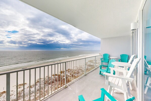 Un balcon avec vue sur la plage et l’océan, des chaises turquoise et une table blanche.