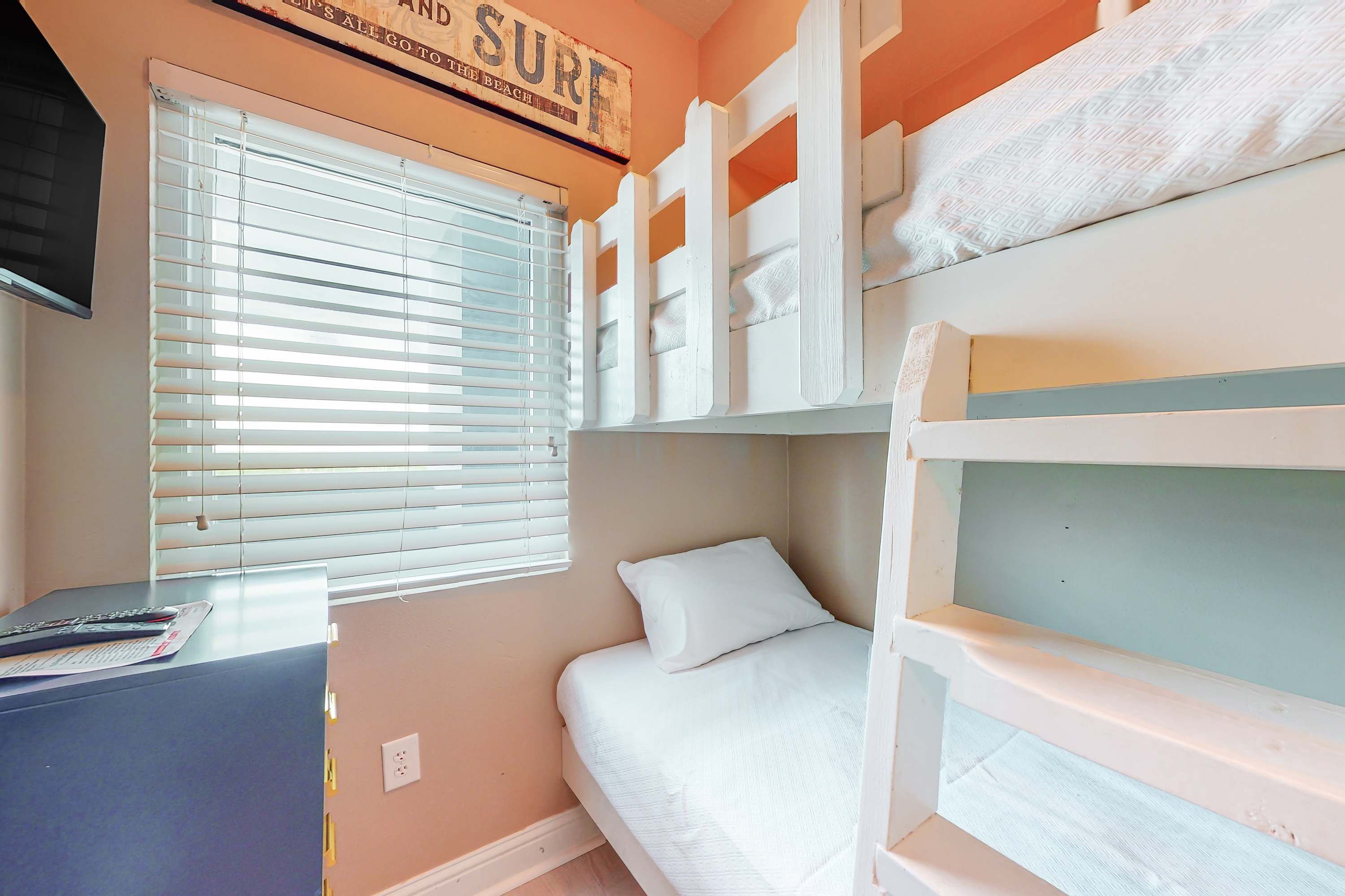 A bunk bed room with a window, a desk with a remote control, and a sign above the window.
