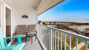 A balcony with a view of the beach, a small table, two chairs, and a sign on the wall. - Gulfview condo with shared pools, sauna, and beach access (Gulf Shores)