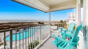 A balcony with a view of a swimming pool and beach, turquoise chairs, and a white building in the background. - Gulfview condo with shared pools, sauna, and beach access (Gulf Shores)