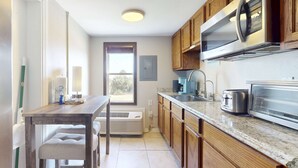 Cozinha com armários de madeira, micro-ondas de aço inoxidável, torradeira e janela com vista.