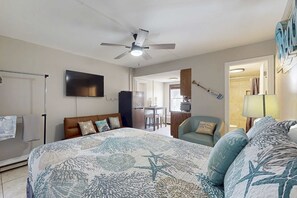 Un dormitorio con una cama, ventilador de techo, televisor, escritorio y una silla.