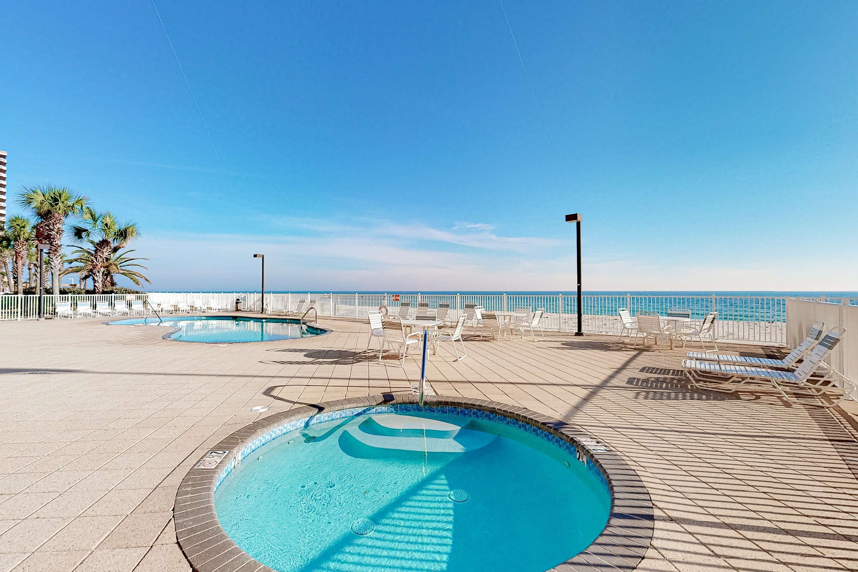A pool area with lounge chairs and a view of the ocean.
