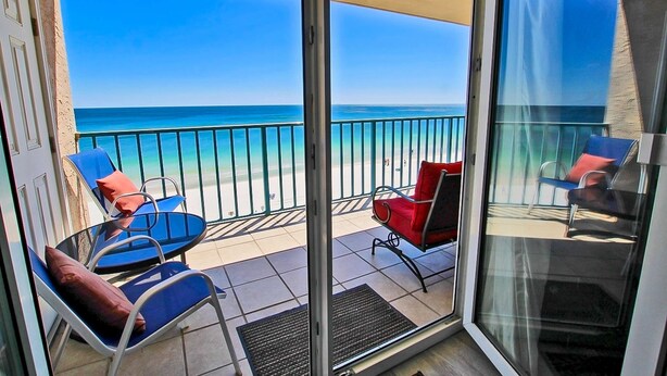 A balcony with a view of the sea, two blue chairs with red cushions, and a red chair. - Oceanfront condo with pool, elevator, well-equipped kitchen, balcony, & W/D (Gulf Shores)