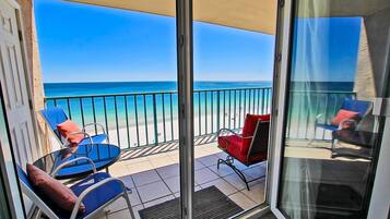 A balcony with a view of the sea, two blue chairs with red cushions, and a red chair.