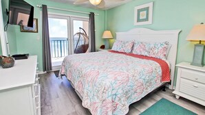 A bedroom with a bed, a ceiling fan, a desk, a chair, a hanging chair, and a view of the outdoors. - Oceanfront condo with pool, elevator, well-equipped kitchen, balcony, & W/D (Gulf Shores)