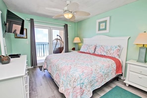 A bedroom with a bed, a ceiling fan, a desk, a chair, a hanging chair, and a view of the outdoors. - Oceanfront condo with pool, elevator, well-equipped kitchen, balcony, & W/D (Gulf Shores)