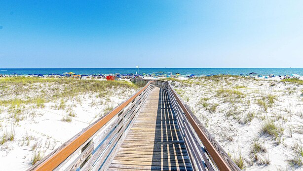 A wooden boardwalk leading to a beach with umbrellas and beach chairs. - 6th-floor beach-view condo with outdoor pool, tennis court, sauna, hot tub, gym (Gulf Shores)