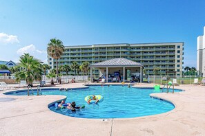 A swimming pool with multiple lanes, a covered seating area, and a large building with balconies in the background. - 6th-floor beach-view condo with outdoor pool, tennis court, sauna, hot tub, gym (Gulf Shores)