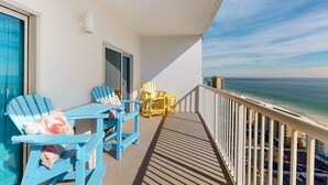 Ein Balkon mit blauen und gelben Stühlen, einem Tisch und Blick auf das Meer.
