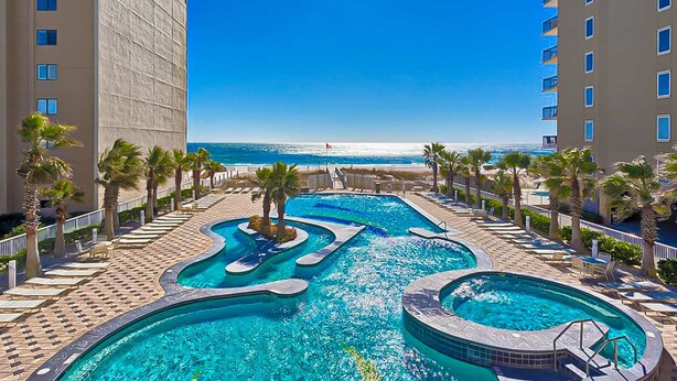 Ein Hotelpoolbereich mit mehreren Schwimmbecken, Palmen und Blick auf den Strand.